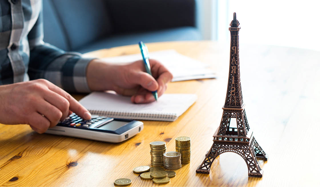 Man counting travel budget, vacation expenses or insurance cost  Traveler planning holiday in Europe  Cheap flights and hotel  Money and little Eiffel Tower souvenir from Paris on table 